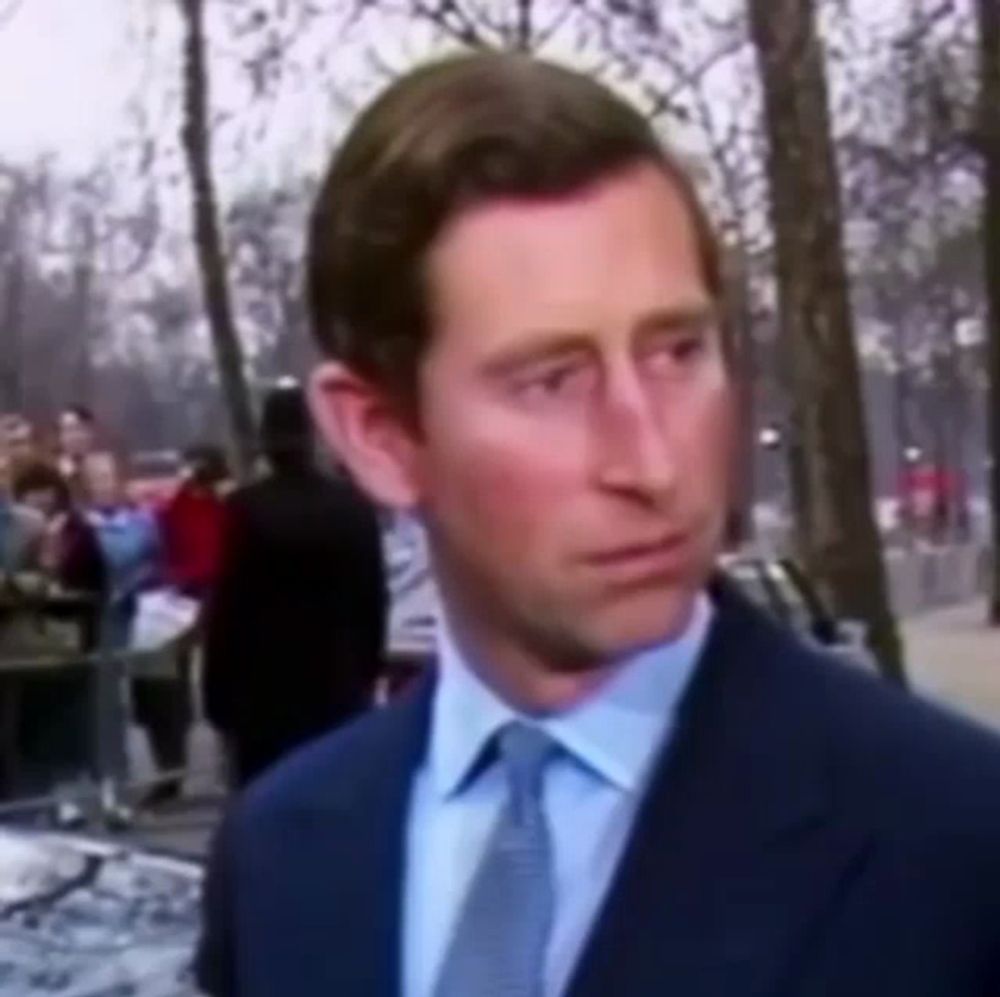 a man in a suit and tie is standing in front of a crowd in a park .