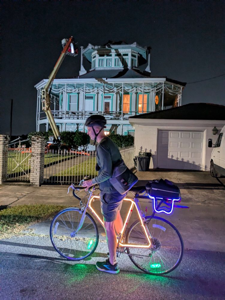 Man on a lit up bike in front of a steamboat house