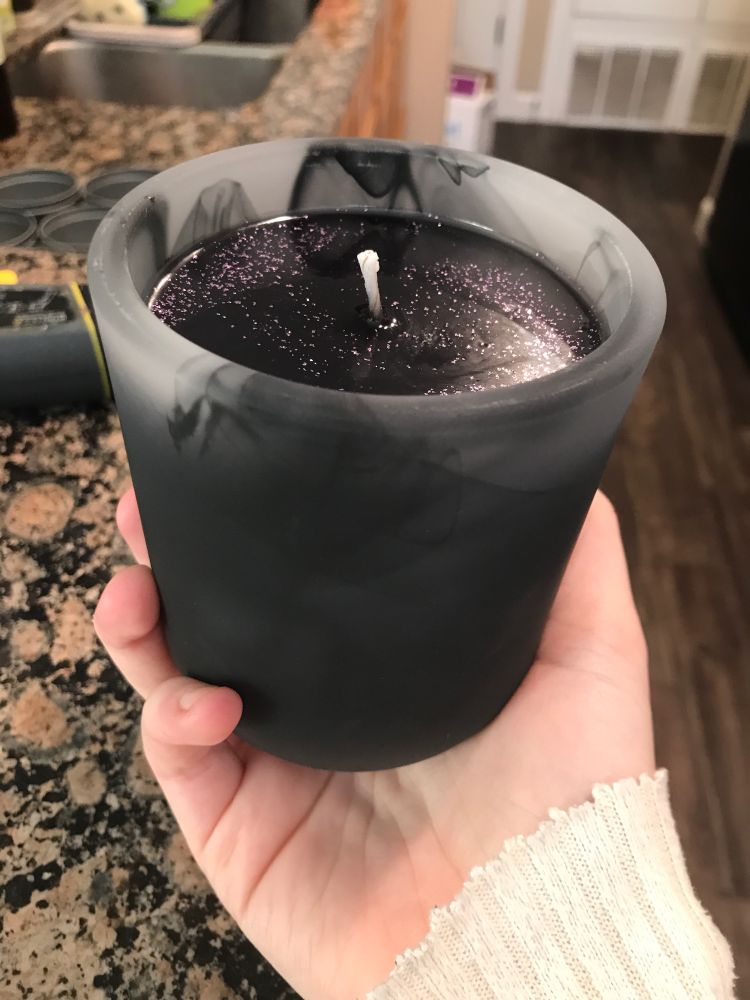 a black candle with purple glitter in a black and gray frosted glass container 