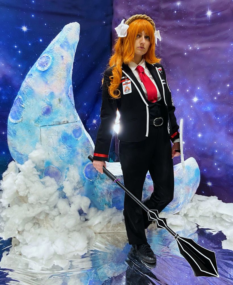 My cosplay of LCB Ishmael. I’m standing in front of a blue moon and purple starry backdrop, holding her mace and shield.
