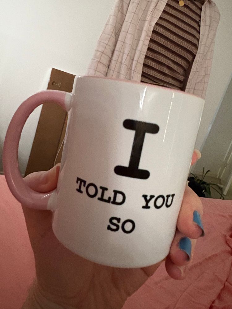 Hand holding a mug with the text ‘I told you so’ written on it. 