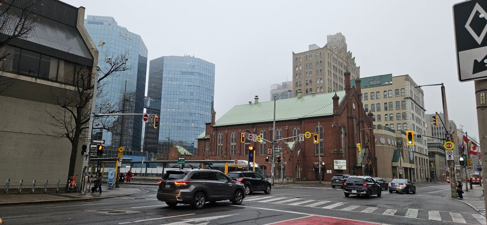 Picture of a busy city intersection with an assortment of buildings, traffic lights, and a crosswalk. It's foggy and grey. 