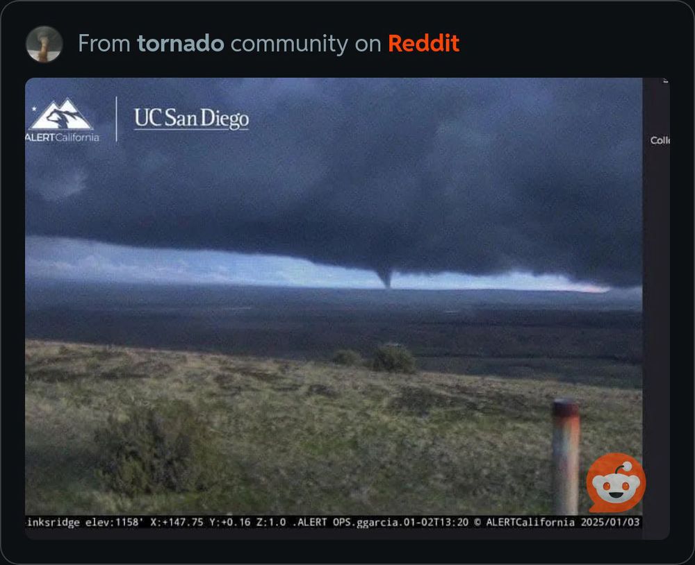 Grey tornado far in the distance underneath a heavy grey mesocyclonic cloud and lighter skies in the background. Scrubby grasslands are in the foreground. From AlertCalifornia and UC San Diego, shared by r/samowarrior on Reddit.