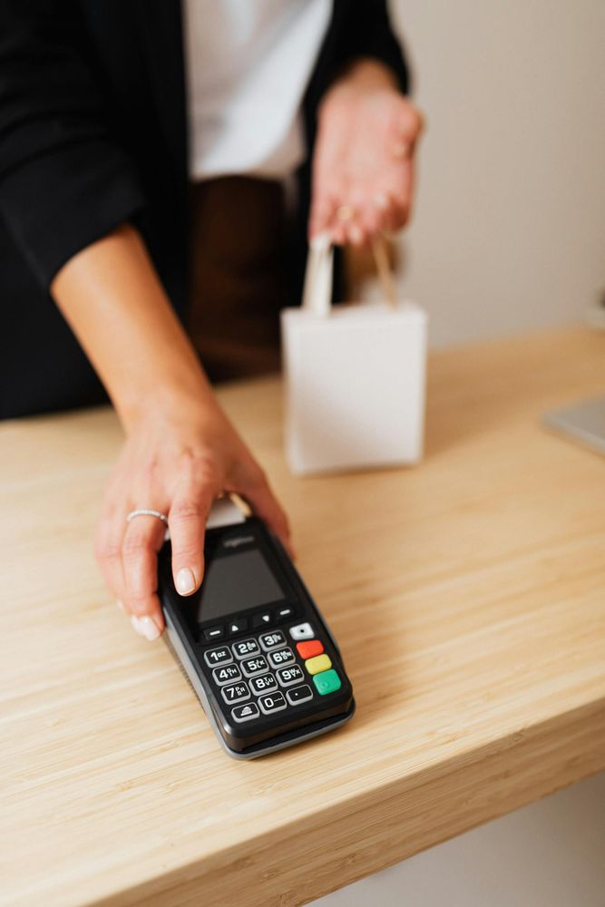 A cashier hands over a payment terminal, while holding a small bag.