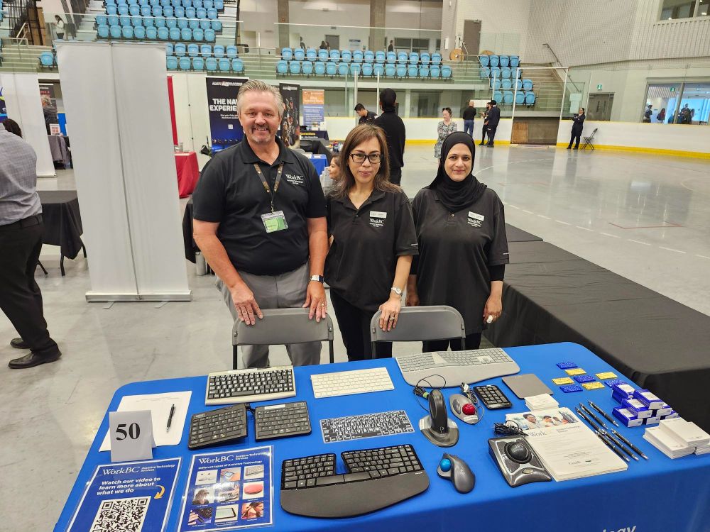 Nate, Joanna, and Andleeb at the WorkBC Assistive Technology Services table with various pieces of assistive technology on display.