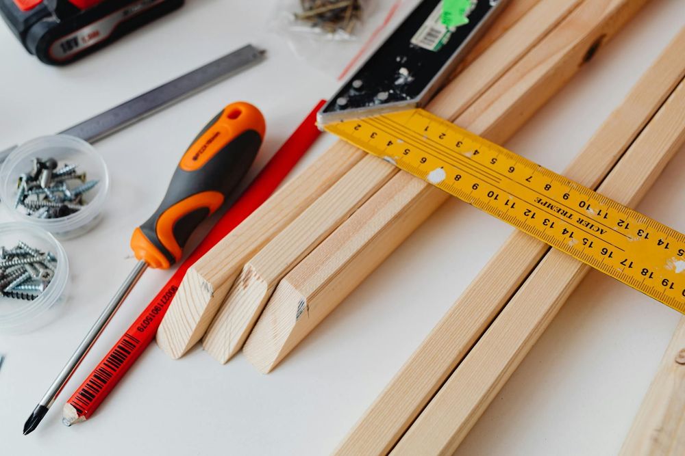 various building supplies including wood, a screwdriver, a ruler, a pencil, and screws