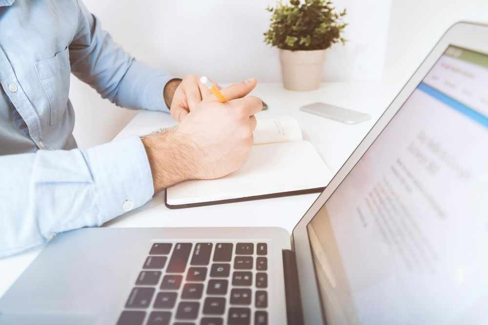 A man writes into a notebook while going on a laptop.