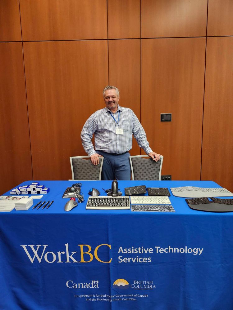 Nate at the WorkBC Assistive Technology Services table with assistive technology on display.