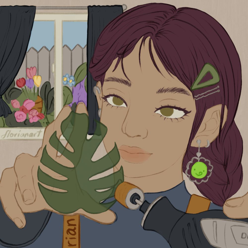 A lapidarist holds an emerald in the shape of a monstera leaf with her right hand. with her left hand, she uses a dremel to sand the sculpture. She is also indoors with a window in the far left background picturing a garden of flowers outside