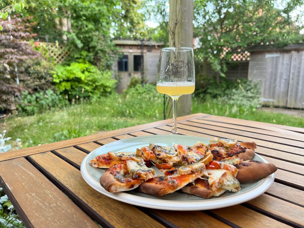 Pizza on a plate and a glass of beer with plants in the background 