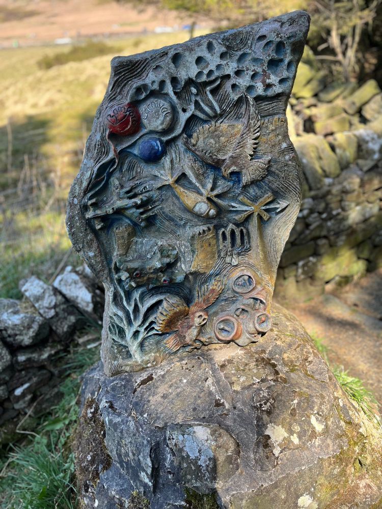 Bamford village carving featuring churches, owls, trees, bells and a Spitfire plane 