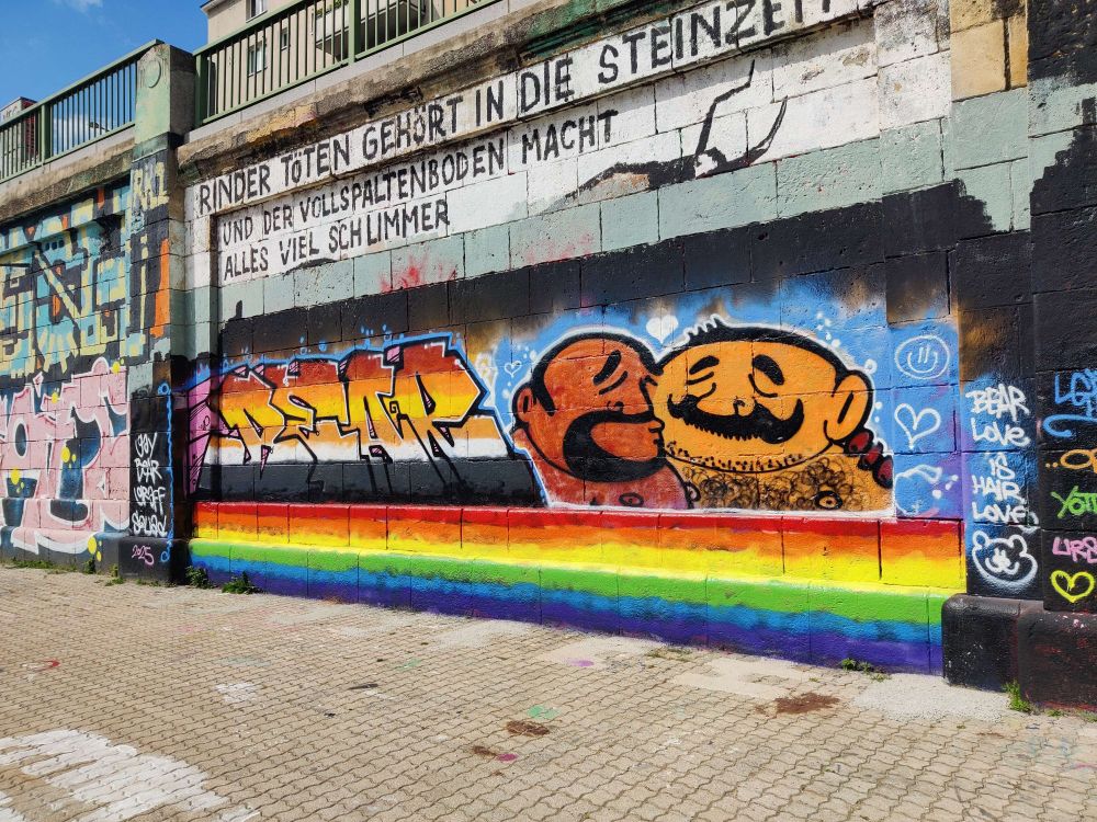 A picture of a graffiti of the word Bear in the bear flag colors in a decorative graffiti font, with a rainbow at the bottom. On the right is a cartoony drawing of two guys kissing. 
There are several little scribbles on the sides of it, one saying "bear love is hair love". 