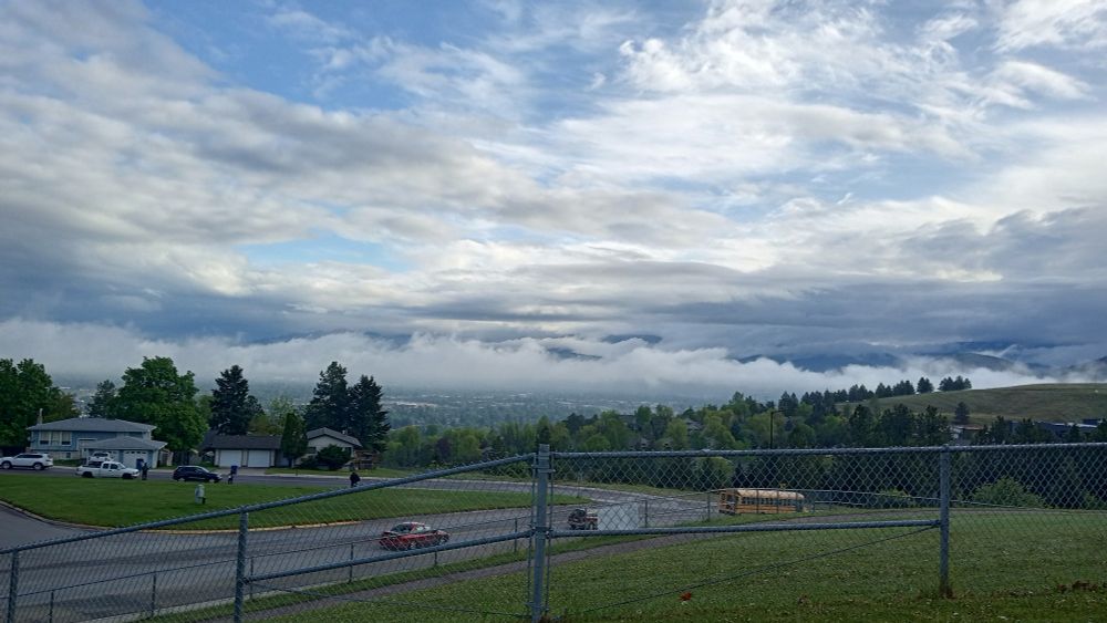 Early morning cloudy blue sky over Missoula city valley from a fenced residential area with houses, cars and pine trees 