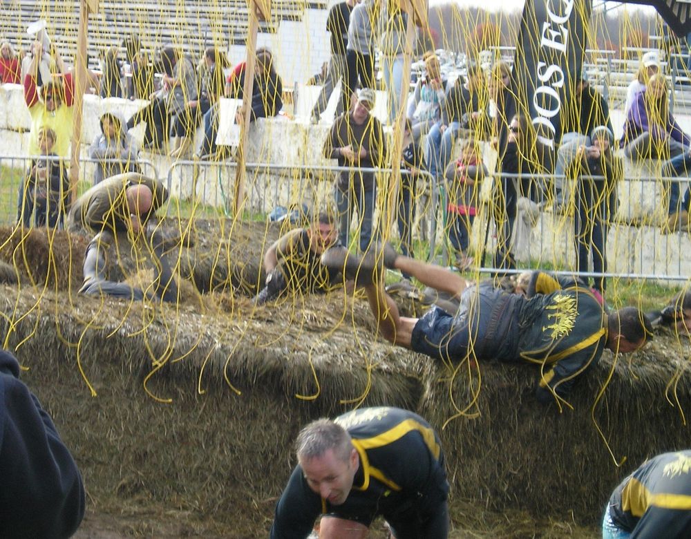 People roll over hay under wires that have 10,000 volts going through them. Perhaps Tough Mudder’s most controversial obstacle, this simple structure remains largely unchanged from its inception and earliest days on course. A field of wires dangling from a rectangular frame, clicking as 10,000 volts crackle through them. Over the years, mud, trenches, rows of hay and even a grandstand have been added to enhance the spectacle. A right of passage for most participants and favorite amongst spectators who enjoy watching the carnage. https://toughmudder.com/obstacles/electroshock-therapy/ 
