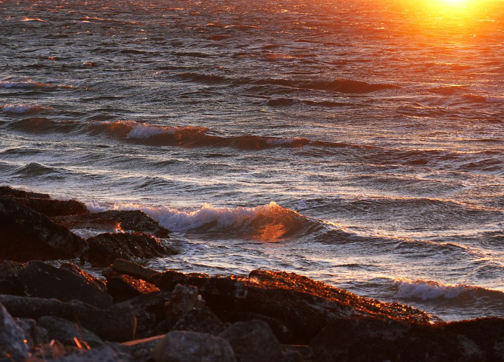 The sunlight dances on the waves and rocks at sunset.