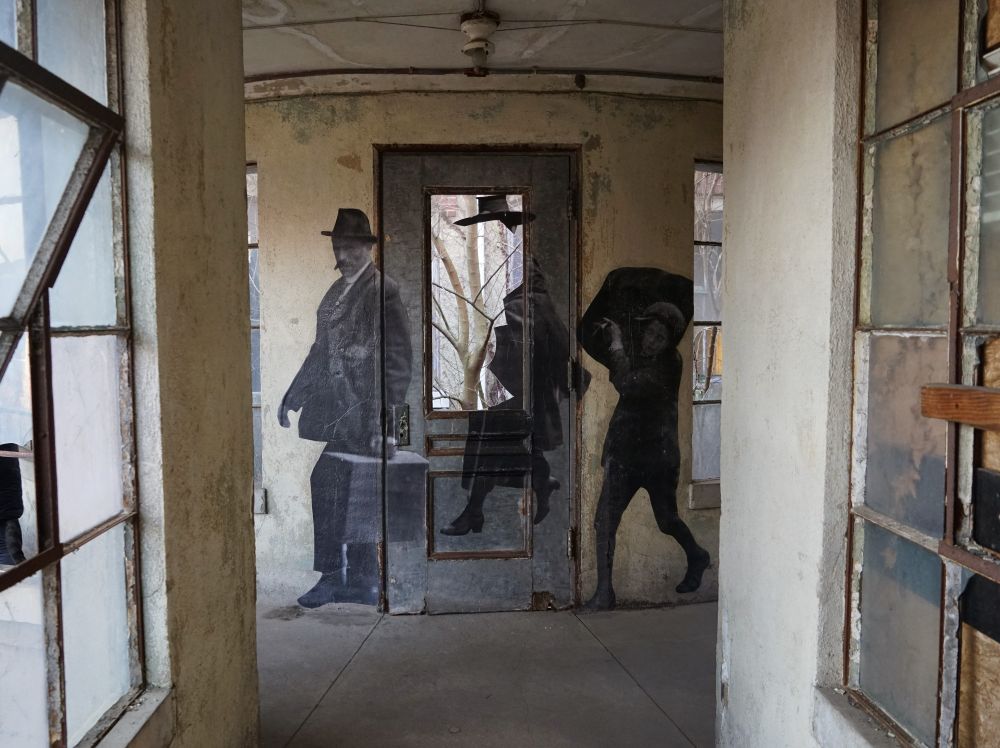 An actual phot from Ellis Island is on the wall. It shoes a man in a hat with a suitcase and a child holding a big bag over his shoulder.