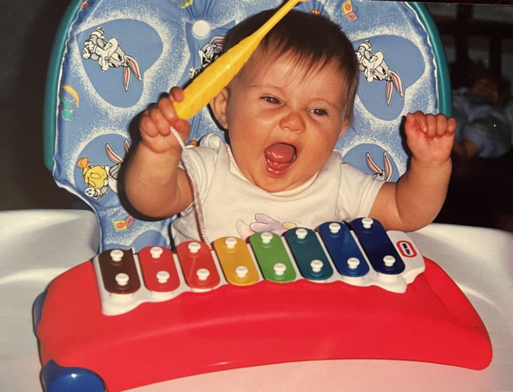 My daughter rocking her Little Tikes Xylophone, both hands are up and she is singing (or yelling lol). Bugs bunny and Tweety are on her chair in light blue hearts
