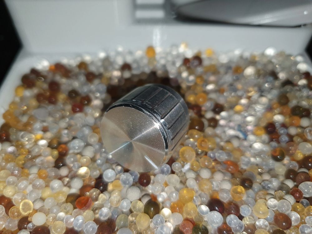A silver knob in multicolored silica gel in a 3d printed white zen garden