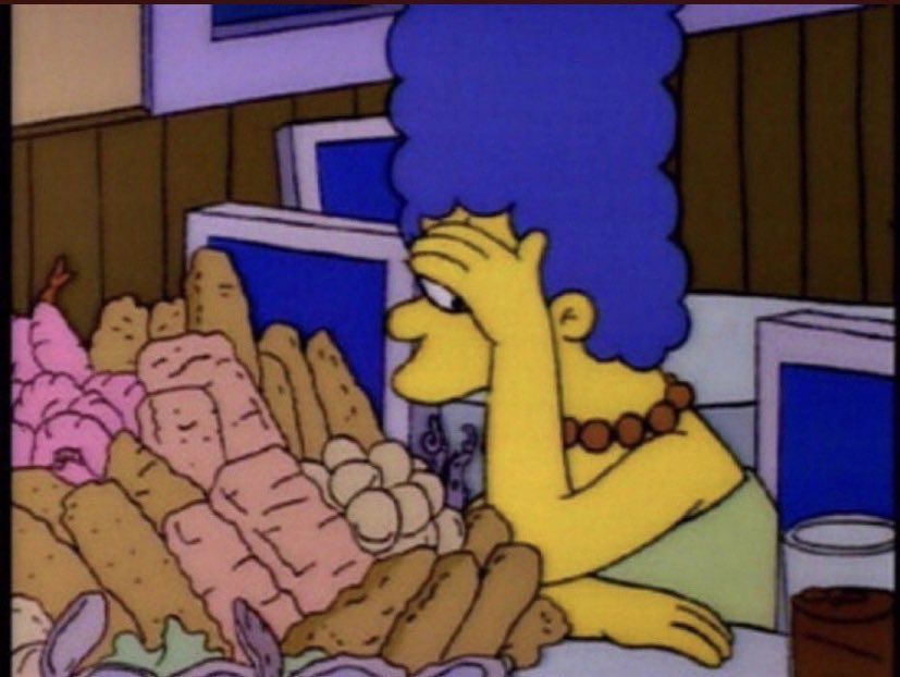 Marge Simpson avergonzada se lleva la mano a la cara en una mesa llena de pan.