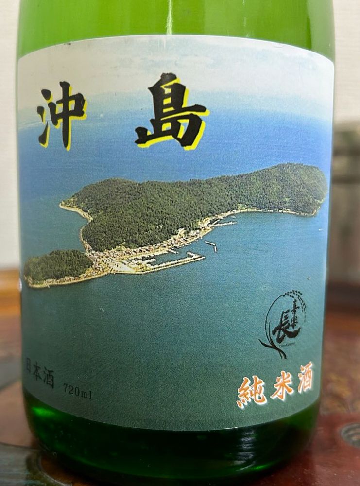 「沖島」というお酒のラベル。青い琵琶湖に浮かぶ、沖島全景の写真が前面にあしらわれている。

右下に喜楽長のロゴマークと純米酒の文字