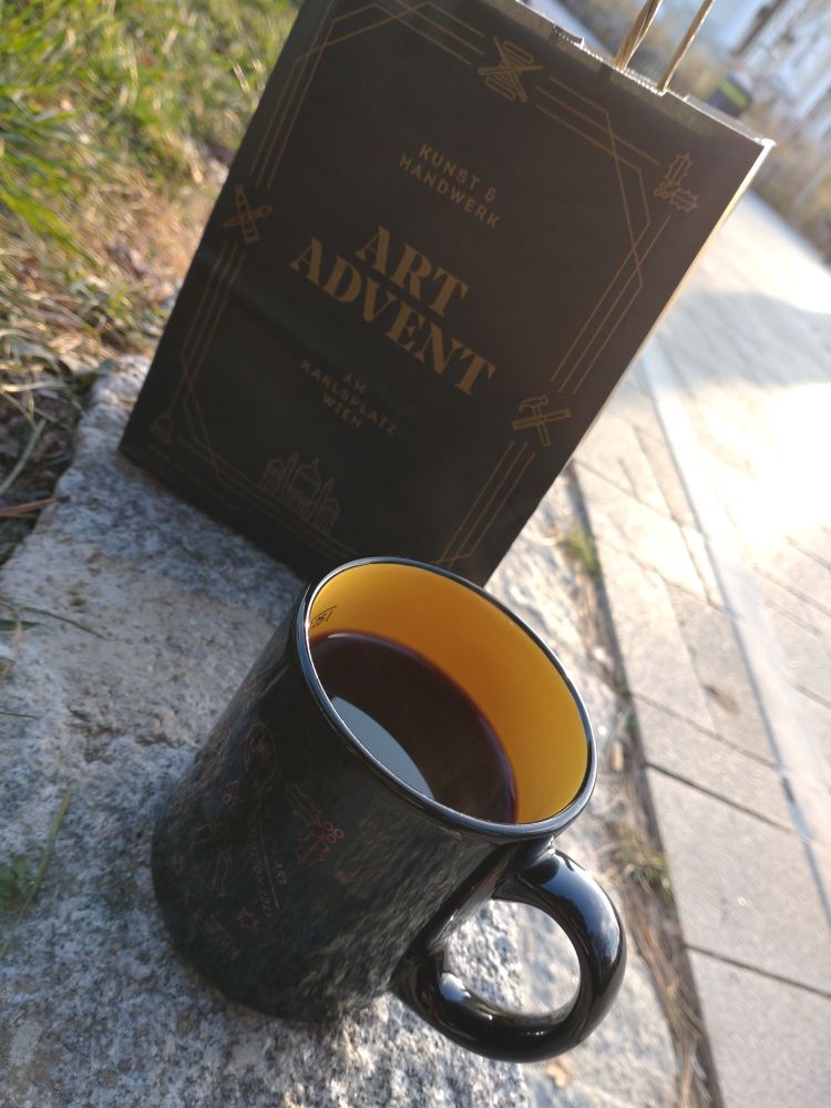 Cup of mulled wine and a paper bag that says Art Advent