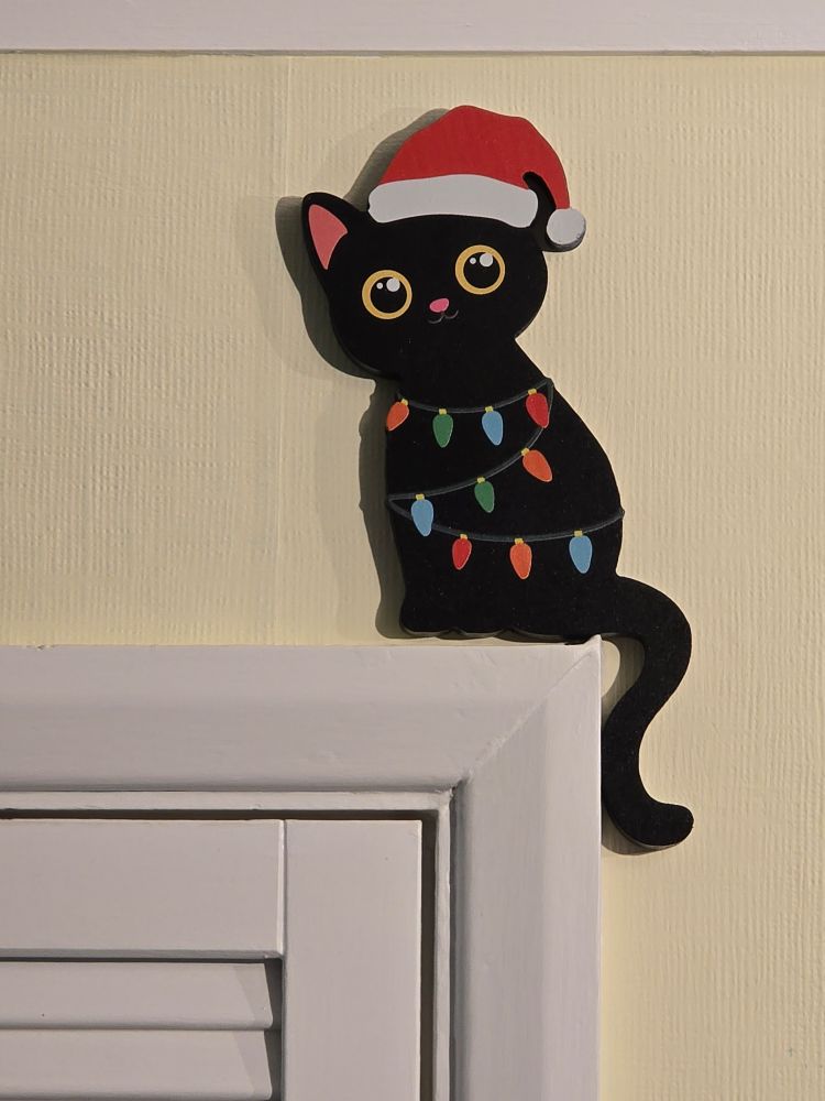A resin cat decoration, wearing a Santa hat and a string of lights. 