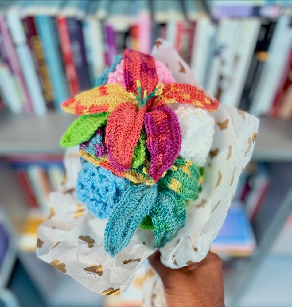 Hand holds up a crocheted rainbow flower bouquet. 