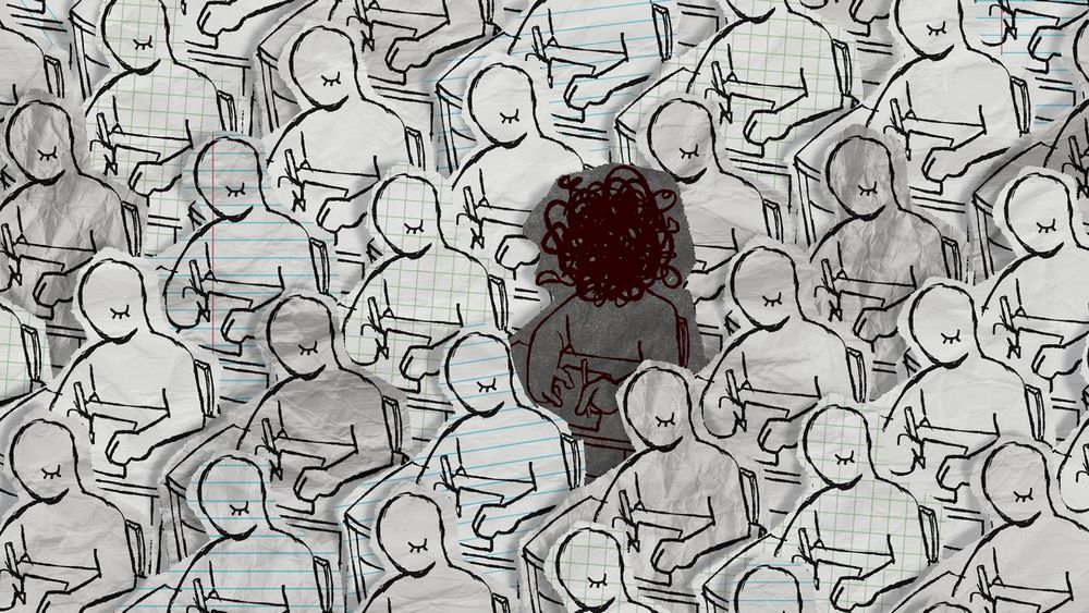 Video game screenshot.

Image shows a room full of people writing at desks. All of the people are featureless except for one closed eye and are made out of different types of paper. In the middle, is one person with a scribbled out face, made out of darker paper.