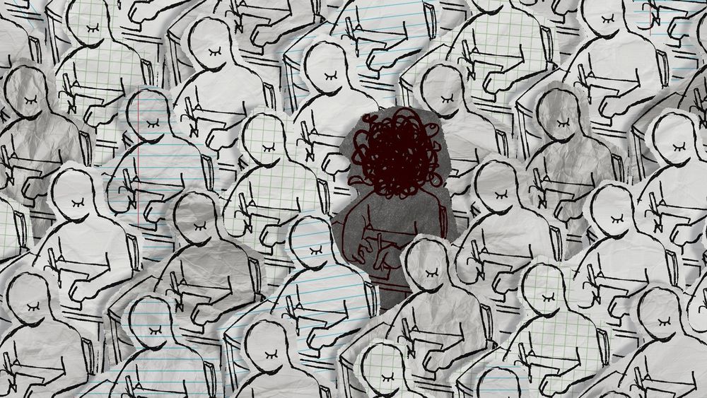 Video game screenshot.

Image shows a room full of people writing at desks. All of the people are featureless except for one closed eye and are made out of different types of paper. In the middle, is one person with a scribbled out face, made out of darker paper.