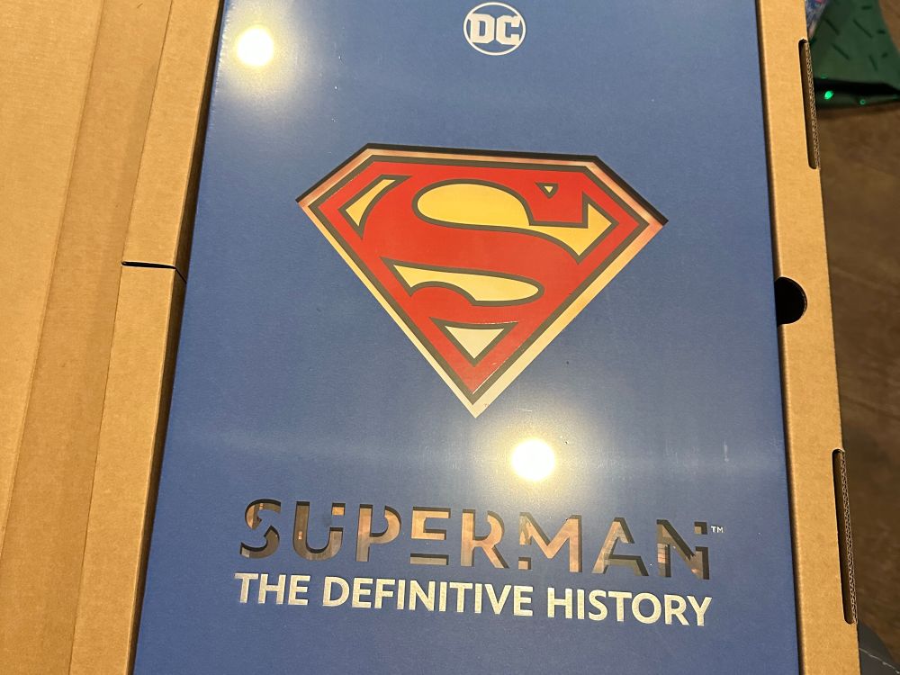 The cover of SUPERMAN: THE DEFINITIVE HISTORY, with the S-shield against a blue background.