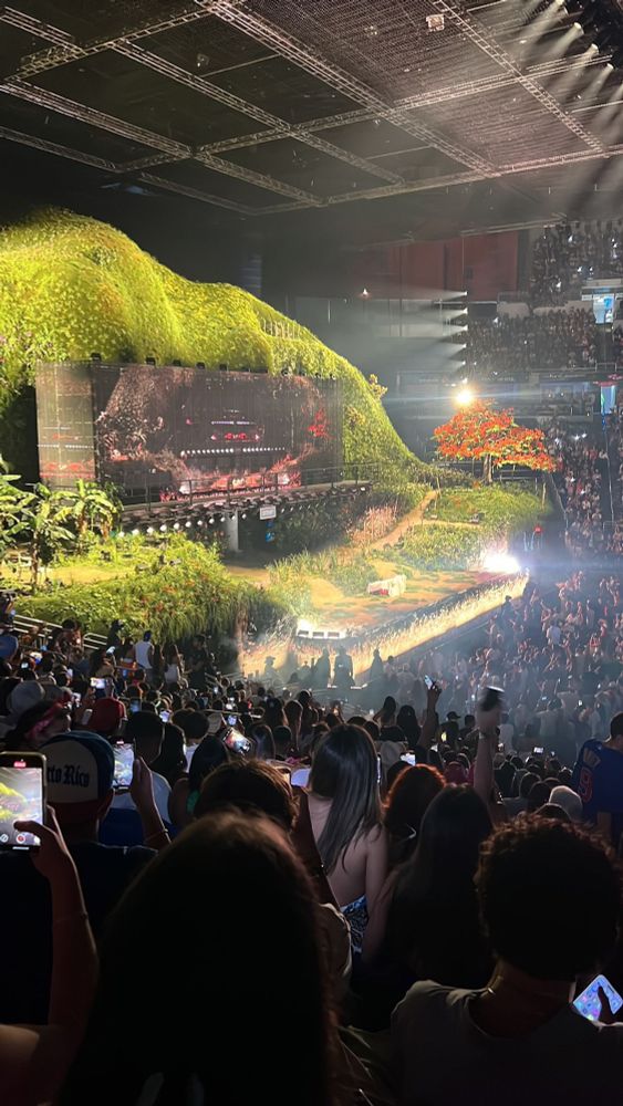 Stage with a grassy hill and giant screen in the middle, audience packed with people 
