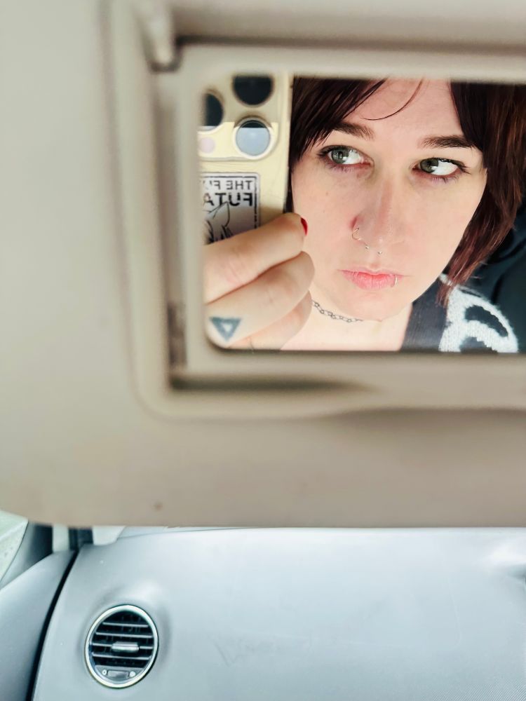 a small mirror selfie of a white girls face with dark hair, light makeup