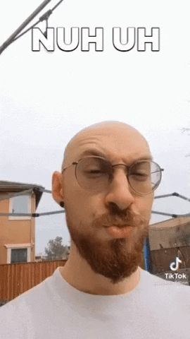 a bald man with a beard and glasses is wearing a white shirt and making a funny face .