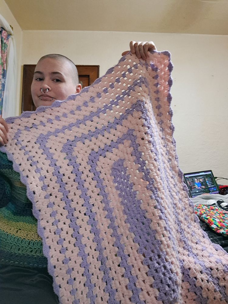 Pickles is holding up a light pink and purple baby blanket