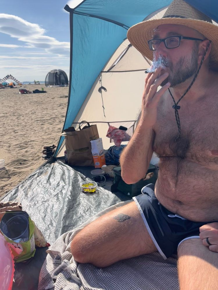 A hairy homosexual in little blue trunks sitting on his knees and smoking a joint
