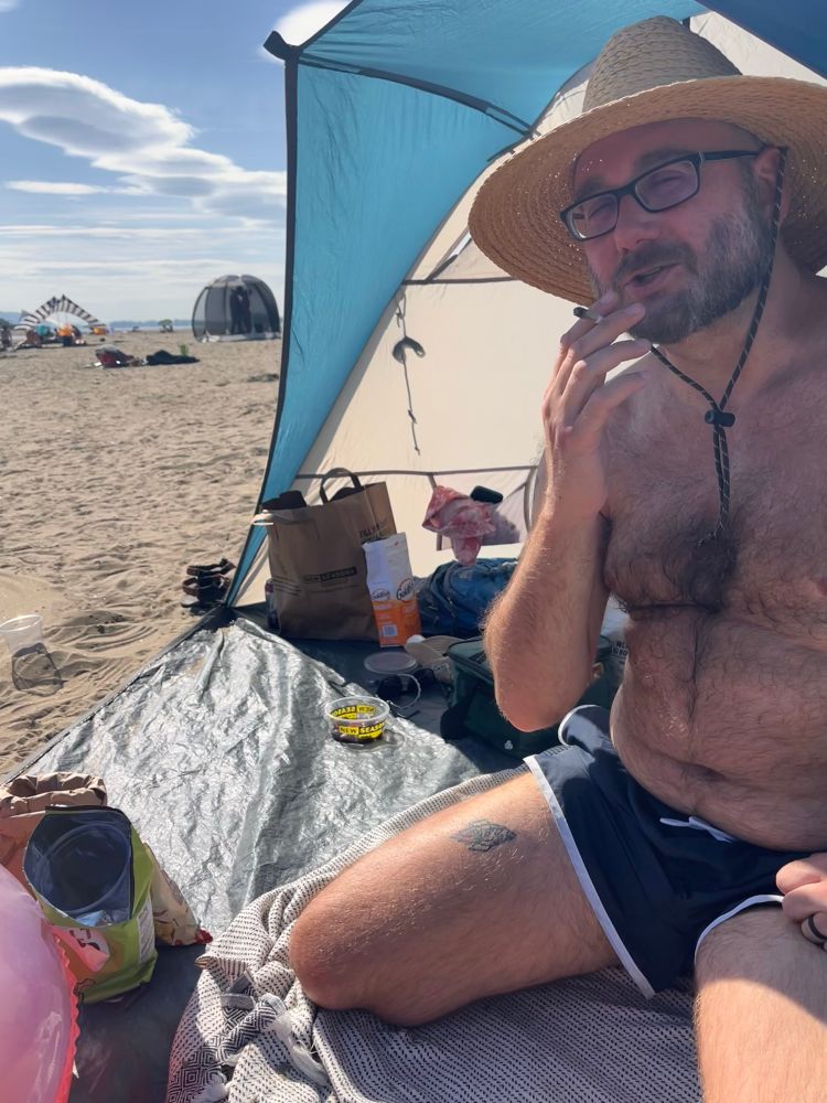 A hairy homosexual in little blue trunks sitting on his knees and smoking a joint