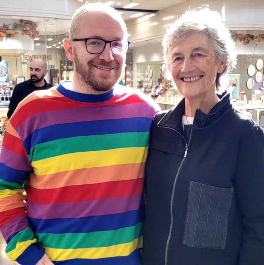 Mike McGrath-Bryan, left, in glasses, with bleached hair and wearing a rainbow jumper, stands for a picture with Irish presidential candidate Catherine Connolly.