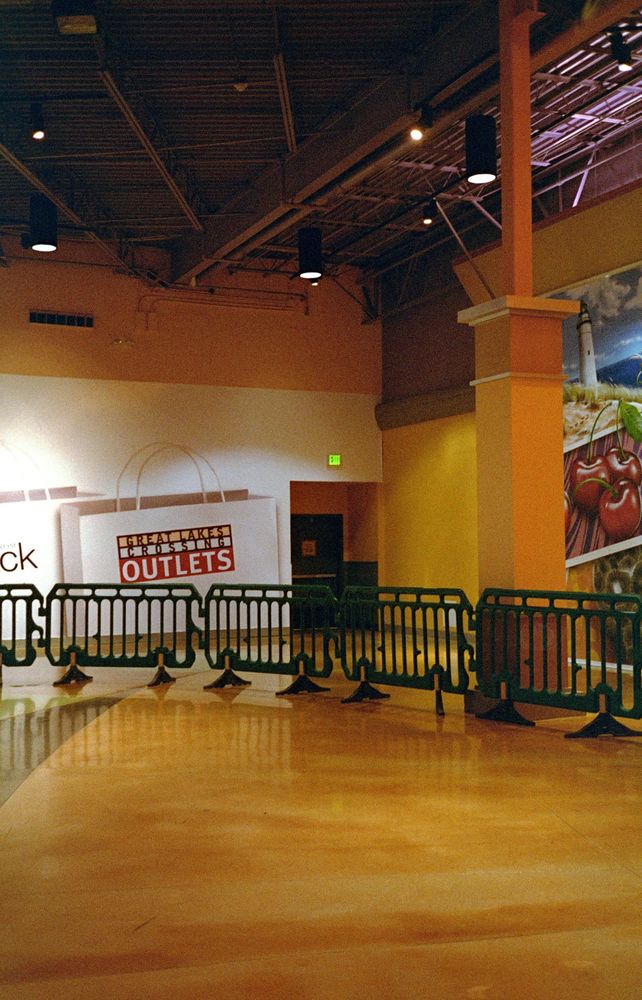 A very empty area in the mall, a green exit sign visible in front of a double door shrouded in shadow