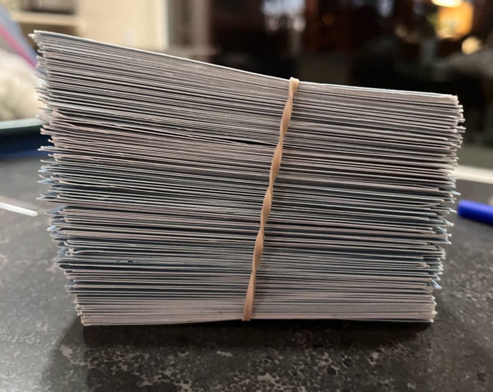 A side view of a stack of postcards held together by a runner band. One side of the stack rises taller than the other.