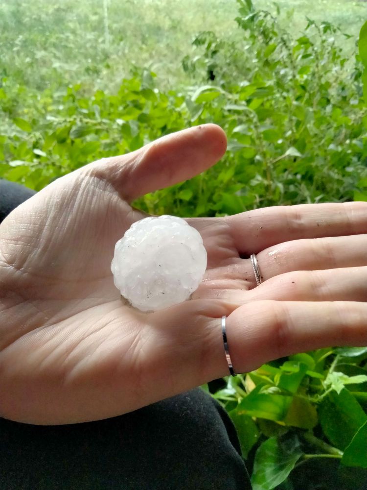Photo d'un grêlon de 3 à 4cm de diamètre posé sur une main. Le fond vert est de l'herbe