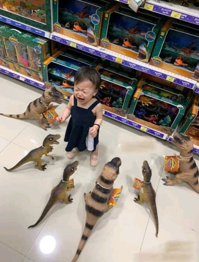 toddler having a meltdown in a store toy isle surrounded by theropod dinosaur toys. 