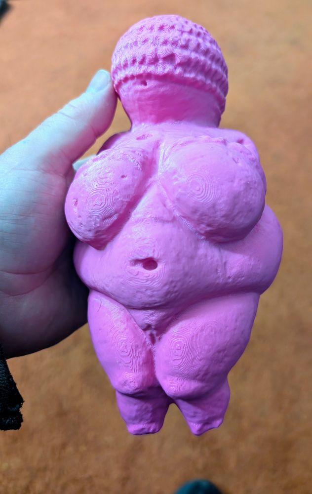 A 3d printed model of the Venus of Willendorf, printed in hot pink with a human hand for scale.