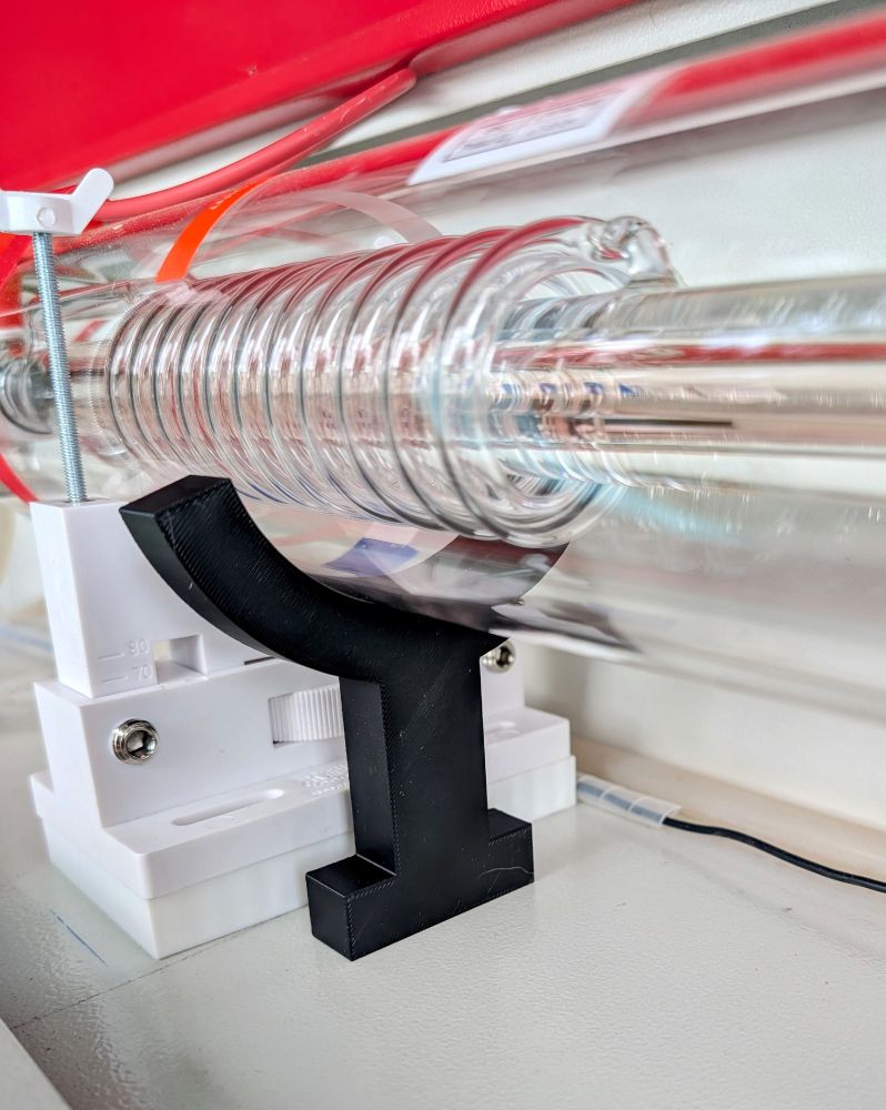 Detail of the anode side of a CO2 laser tube. It shows a white mounting bracket to hold the laser tube. In front of that is a black piece that looks vaguely like the outline of a champagne glass. It is a measuring device to set the height of the laser tube.