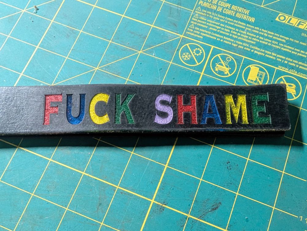 Detail of a BDSM impact toy, a 'slapper' with the words 'fuck shame' laser cut in the leather, and highlighted with paint.