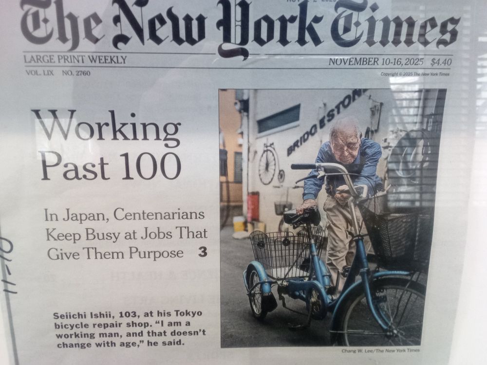 New York Times (Large Print Weekly), headline: WORKING PAST 100, sub-headline: In Japan, Centenarians Keep Busy at Jobs That Give Them Purpose. Photo of an old man with a bicycle, photo caption: Seiichi Ishii, 103, at his bicycle repair shop. "I am a working man, and that doesn't change with age," he said.