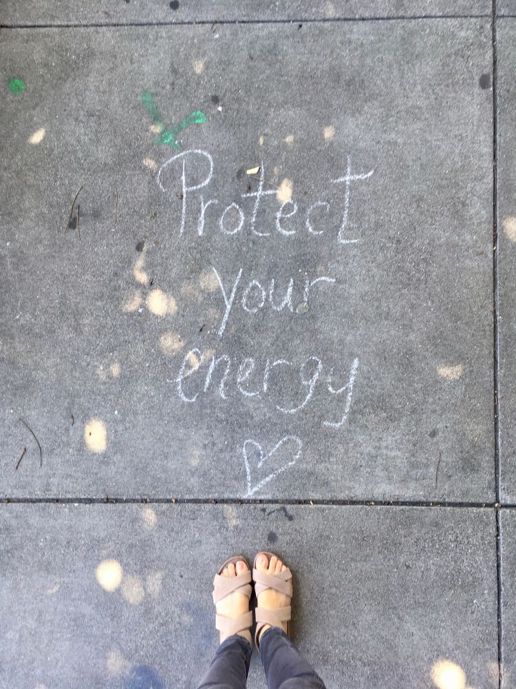 POV looking down at my feet & a chalk message on the sidewalk that says “Protect your energy <3”