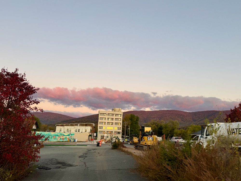 Mountains, mural , pink clouds, CAT equipment, Water truck, debris and scrub growth. 