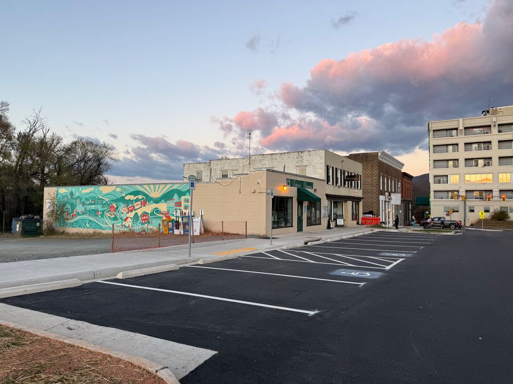 Picture of newly paved parking lot with two newly striped handicapped spaces, plus a mural on the left and clouds above