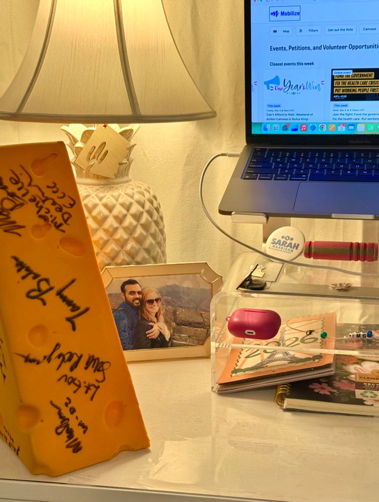 Liz’s cheesehead sits on a desk next to her laptop, which is open to mobilize.us