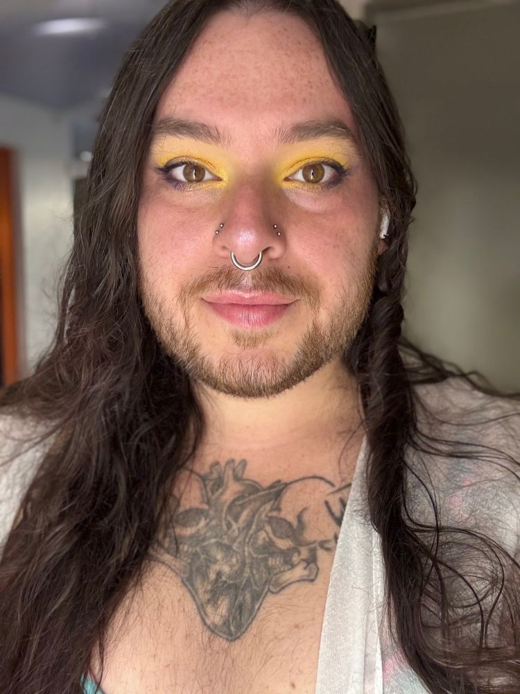Person with long brown hair and a white duster in a selfie with yellow makeup 